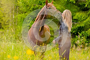 Blonde woman standing in a meadow kissing her arabian horse