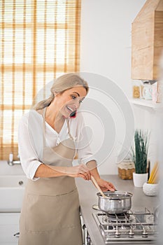 Blonde woman stirring something in a saucepan and talking on the phone