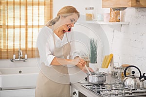 Blonde woman stirring something in a saucepan and talking on the phone