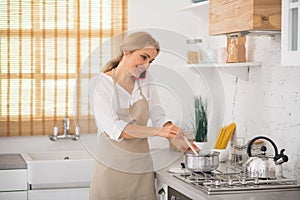 Blonde woman stirring something in a saucepan and talking on the phone