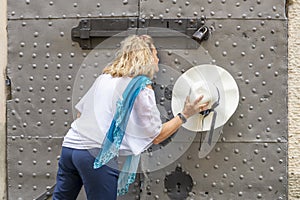 Blonde woman with a straw hat in her hand spies from the keyhole of an ancient door