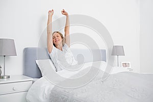 Blonde woman stretching her arms in bed in the morning