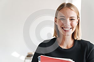 Blonde woman student indoors holding copybooks