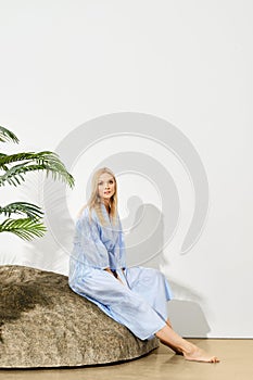 Blonde woman in summer dress sits on rock