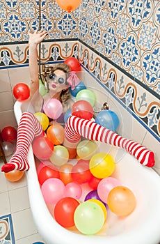 Blonde woman with sunglasses playing in her bath tube with bright colored balloons. Sensual girl with white red striped stockings