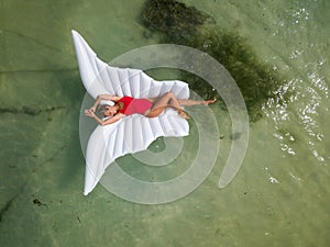 Beautiful and sexy, attractive woman in red swimsuit lays on wing shaped inflatable air mattress floating on water. photo