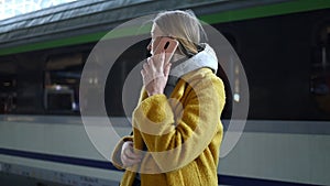 Blonde woman talking on mobile phone at train station. 4K. Girl calling by a smart phone while waiting for a train