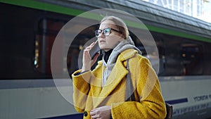 Blonde woman talking on mobile phone at train station. 4K. Girl calling by a smart phone while waiting for a train