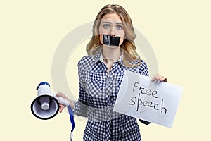 Blonde woman with taped mouth holding megaphone and banner with silence inscription.