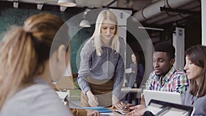 Blonde woman team leader giving direction to mixed race team of young guys. Creative business meeting at modern office.