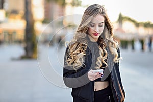 Blonde woman texting with her smartphone in urban background