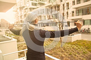 Blonde woman training resistance band arm workout in balcony at home