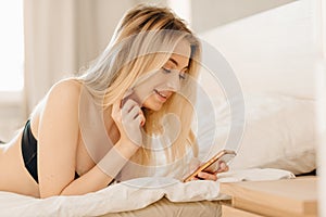 Blonde woman using her smartphone as she staying in bed at her day off