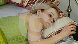 Blonde woman wakes up, looks at alarm clock and hides it under the pillow. 4K