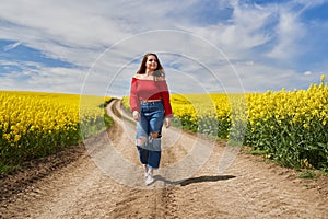 Blonde woman walking on a road through a canola field