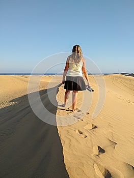 blonde woman walking at the top of a dune while looking the sea on the horizon at the sunset. Walking the barefoot girl is shaping