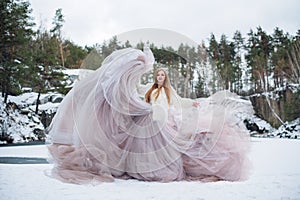 Blonde woman in waving dress in winter outdoors. Fabric flying and fluttering. Fashion model in long waving gown dancing on frozen