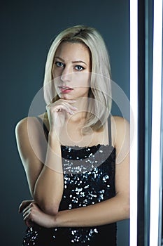 Blonde woman wearing elegant black sequin strap cami dress standing on dark interior