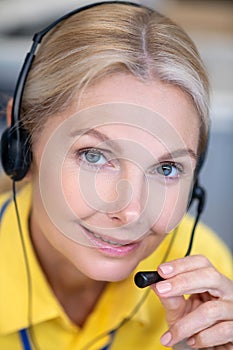 Blonde woman wearing headphones, speaking into microphone, looking into camera