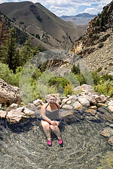 Blonde woman wearing a polka dot swimsut soaks and enjoys the Goldbug Hot Springs in the Salmon Challis National Forest of Idaho