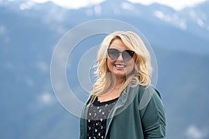 Blonde woman wearing sunglasses poses for a portrait with the Cascade Mountains in background