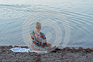 Blonde woman wearing a swimsuit coverup sits on the shores of Lake McDonald photo