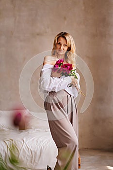 a blonde woman in a white shirt and a bouquet of peonies.