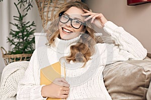 Blonde woman in white woolen sweater and glasses reading book