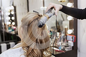 A blonde woman is wound a lock of hair on a curling iron in a professional beauty salon. Close-up
