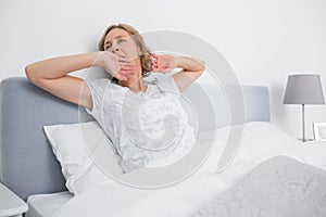 Blonde woman yawning and stretching in bed in the morning