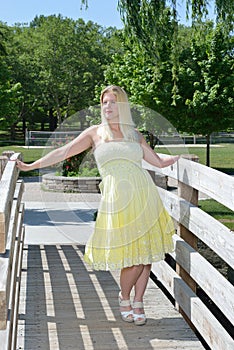 Blonde woman in yellow sundress poses on bridge