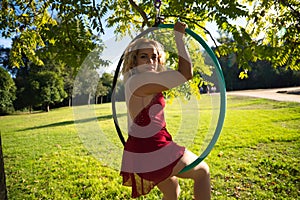 Blonde woman and young gymnast acrobat athlete performing aerial exercise on air ring outdoors in park. Flexible woman in red
