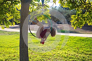 Blonde woman and young gymnast acrobat athlete performing aerial exercise on air ring outdoors in park. Flexible woman in red