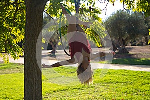 Blonde woman and young gymnast acrobat athlete performing aerial exercise on air ring outdoors in park. Flexible woman in red