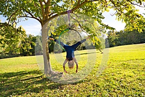 Blonde woman and young gymnast acrobat athlete performing aerial exercise on air ring outdoors in park. Lithe woman in blue