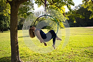 Blonde woman and young gymnast acrobat athlete performing aerial exercise on air ring outdoors in park. Lithe woman in blue