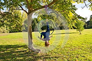 Blonde woman and young gymnast acrobat athlete performing aerial exercise on air ring outdoors in park. Lithe woman in blue