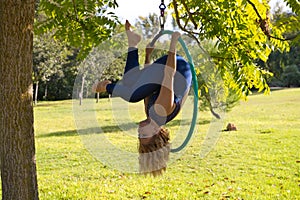 Blonde woman and young gymnast acrobat athlete performing aerial exercise on air ring outdoors in park. Lithe woman in blue