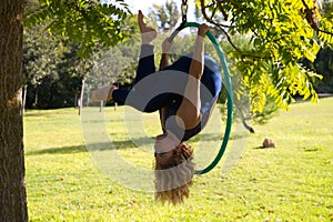Blonde woman and young gymnast acrobat athlete performing aerial exercise on air ring outdoors in park. Lithe woman in blue