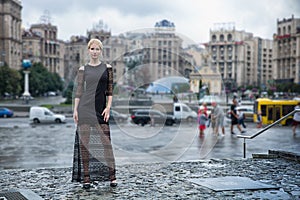 Blonde wooman dreesed in black dress in the city. Rainy day.