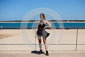 Blonde, young and beautiful woman dressed in black skirt and black top is on the promenade of the sea. The girl is doing different