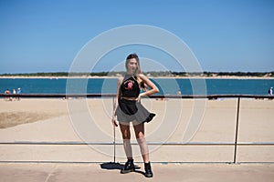 Blonde, young and beautiful woman dressed in black skirt and black top is on the promenade of the sea. The girl is doing different