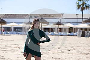 Blonde, young and beautiful woman dressed in an elegant green dress, standing on the seashore and doing different body poses. In