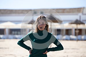 Blonde, young and beautiful woman dressed in an elegant green dress, standing on the seashore and doing different body poses. In