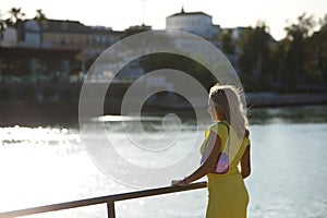 Blonde, young and beautiful woman leaning on the railing on the riverside promenade in seville looking at the skyline. The woman