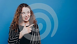 Blonde young excited woman exclaiming and pointing finger upward isolated over blue background