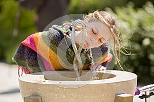 Blonde young girl drinks at public fountain