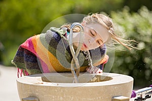 Blonde young girl drinks at public fountain