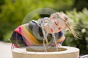 Blonde young girl drinks at public fountain