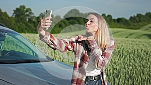 Blonde, young lady wearing plaid shirt and jeans, taking selfie.